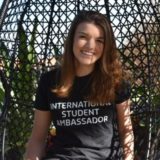 Curtin student, Melina Schuett sitting in a swinging chair, wearing a black Curtin International student ambassador shirt, looking at camera and smiling