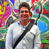 Curtin student Dean Bussanich leaning against a colourful wall, looking at camera and smiling