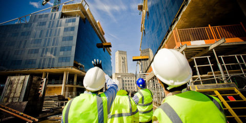 Group of industrial workers, wearing high-vis and hard hats, walking around buildings