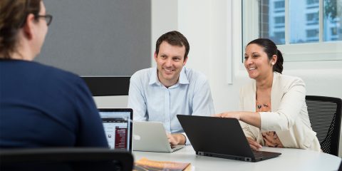 Three business students sitting at a table discussing what's on their laptops