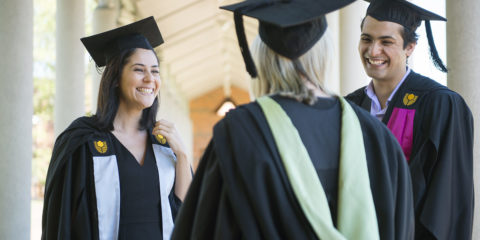 Two female students and a male student standing around talking, wearing graduation gowns