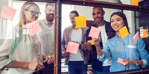 A group of people sticking colourful post-it notes on a glass window